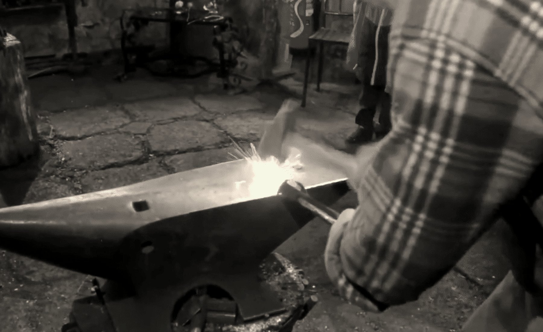 Métal incandescent travaillé à la forge, gerbe d'étincelles dans l'atelier